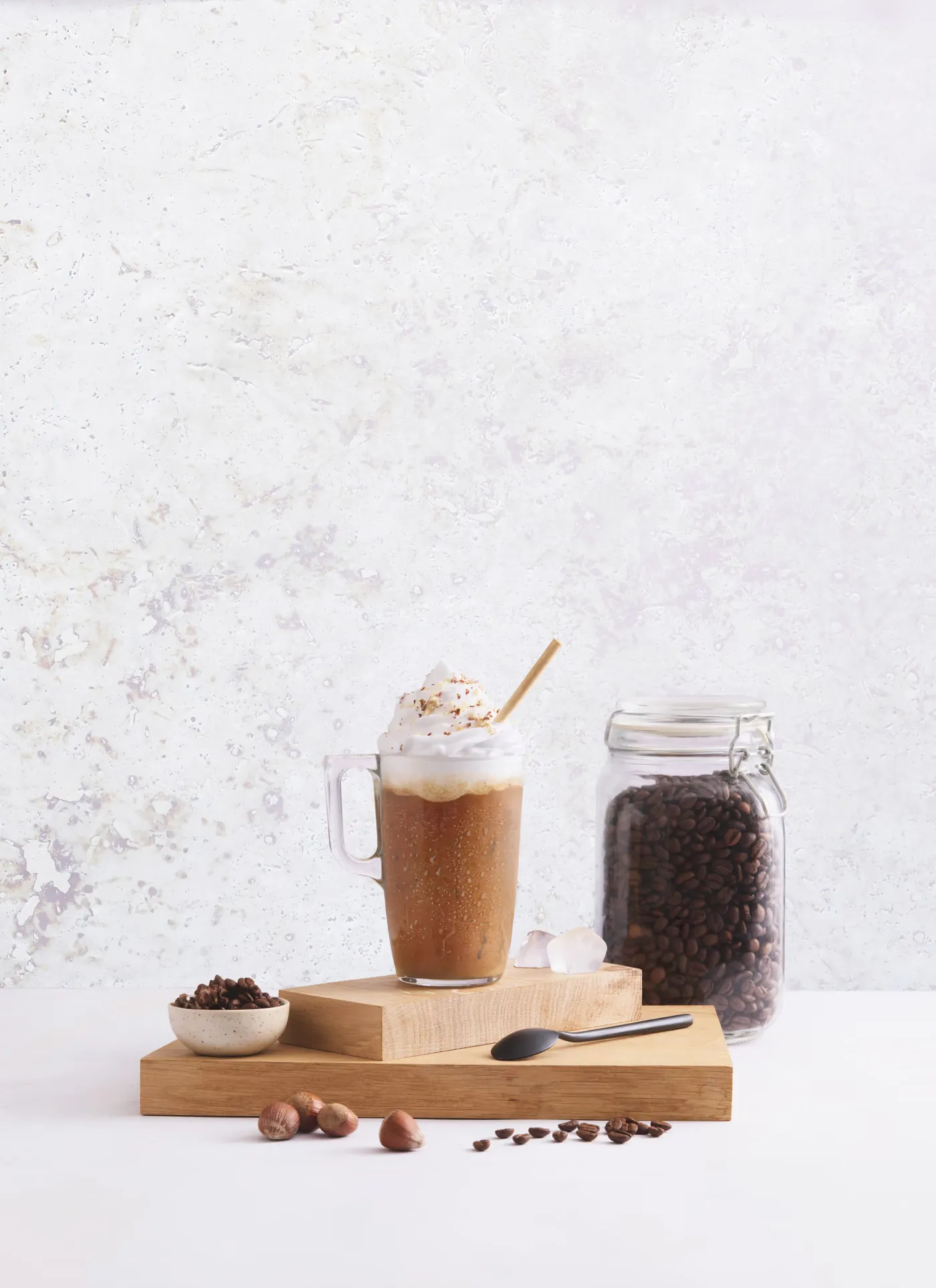 Café frappé surmonté de chantilly, à côté d’un bocal de grains de café