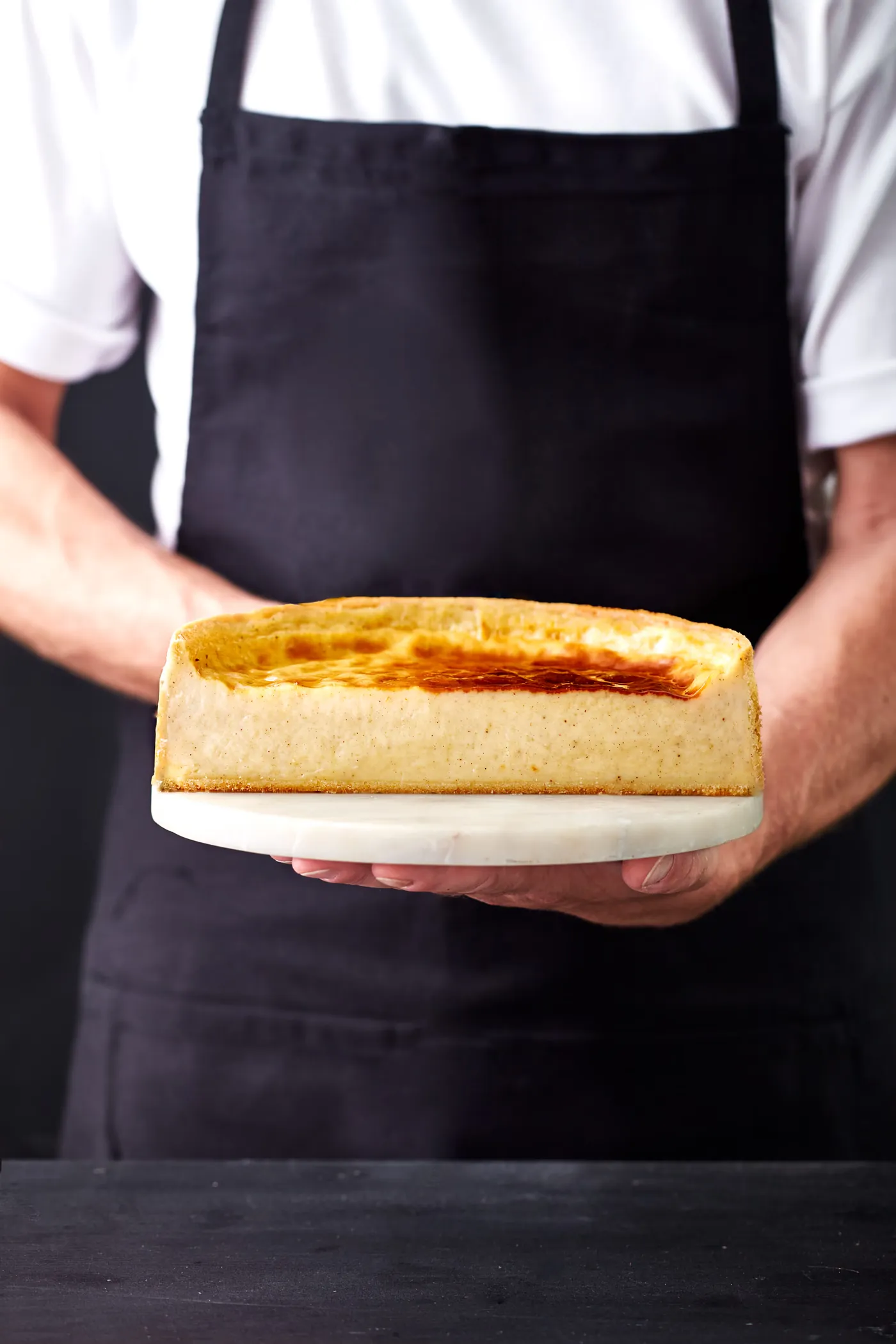 Cheesecake entier présenté par un pâtissier en tablier