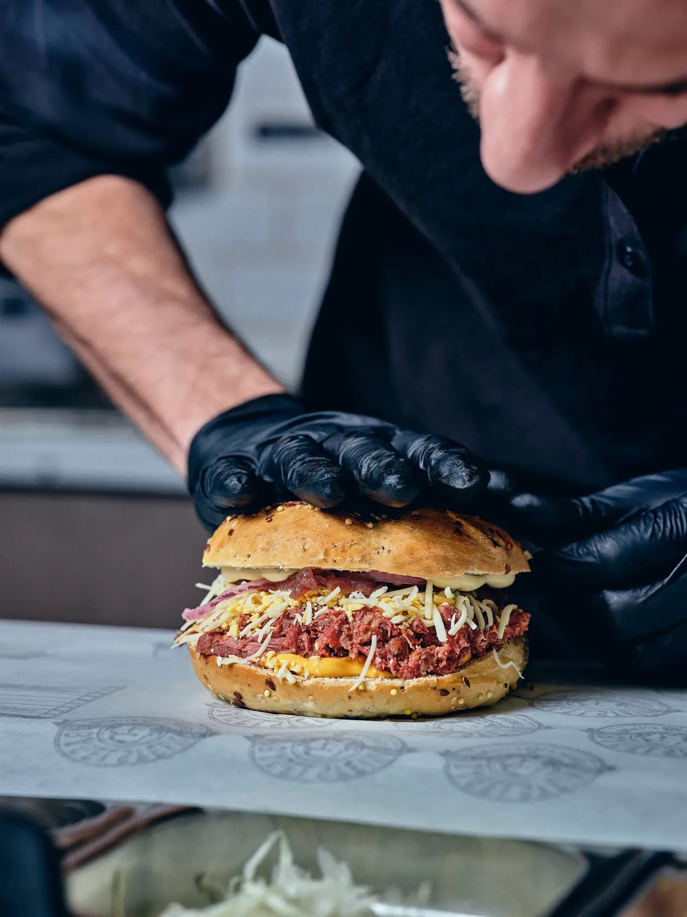 Un équipier referme un bagel pastrami derrière le comptoir