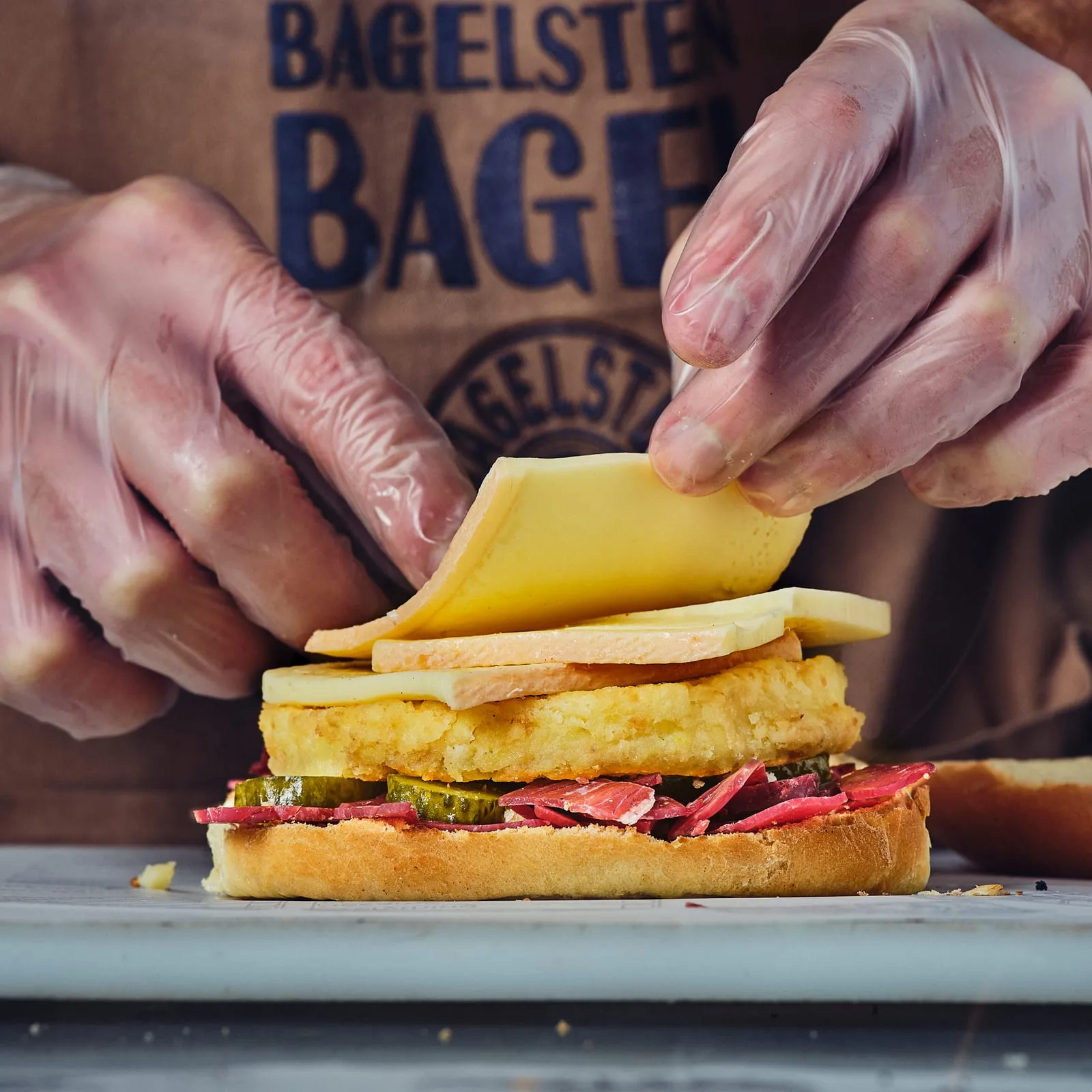 Assemblage d'un bagel Bagelstein : tranche de raclette posée sur le poulet crispy